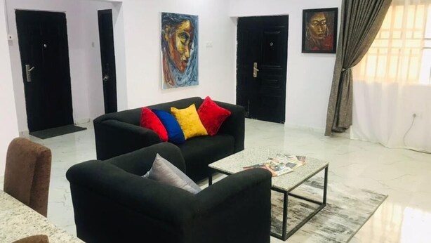 Una sala de estar moderna con un sofá negro, cojines coloridos, una mesa de centro y obras de arte en las paredes.