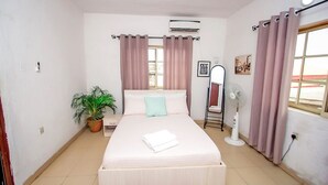 Un dormitorio con cama, cortinas, un ventilador, una planta en maceta y una ventana.
