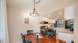 A modern kitchen with white cabinets, stainless steel appliances, and a wooden dining table with chairs. - Renton Oasis-Relaxing 3BR Home with Great Outdoor (Renton)