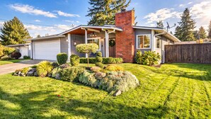 A modern two-story house with a garage, a brick chimney, and a well-maintained front yard with shrubs and a small tree. - Renton Oasis-Relaxing 3BR Home with Great Outdoor (Renton)