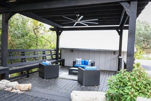 Estarão ao ar livre coberto com ventilador de teto, mobiliário de vime preto e vista para o verde ao redor.