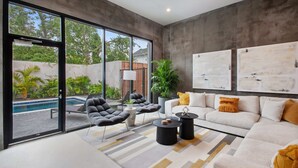 A modern living room with a large sliding glass door leading to a pool, a white sofa with yellow cushions, black armchairs, and a coffee table. - Claudia - Unit 5 | Sense of Calm and Relaxation, Walking Distance to the Excitem (New Orleans)