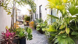 A narrow brick pathway flanked by lush green plants and a white building with a black door. - Claudia - Unit 4 | Sense of Calm and Relaxation, Walking Distance to the Excitem (New Orleans)