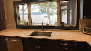A kitchen with a large window, a sink, and dark cabinets. - Lake & Mountain Retreat - Summer Adventures & Winter Escape (Center Ossipee)