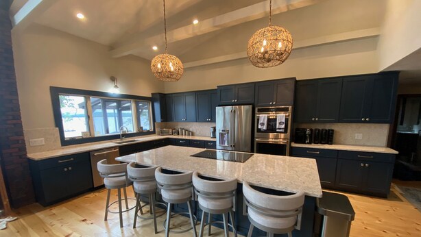 A modern kitchen with dark cabinetry, stainless steel appliances, and a central island with bar stools. - Lake & Mountain Retreat - Summer Adventures & Winter Escape (Center Ossipee)