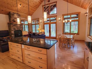 A spacious kitchen with a stone fireplace, wooden ceiling, and large windows.