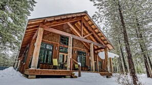 Une cabane en rondins avec une façade en bois, de grandes fenêtres et une véranda avec des chaises.