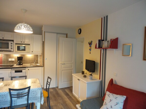 A compact kitchen with a dining area, a small TV, and a cozy seating area with a red cushion.