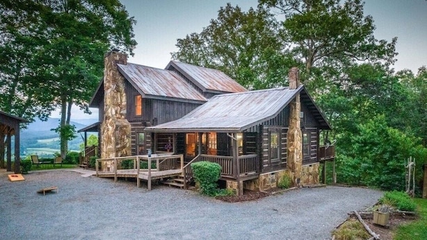 A rustic cabin with a stone exterior, wooden deck, and a gravel driveway.