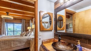 A wooden cabin room with a bed, a large mirror, and a wooden countertop with a sink.