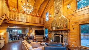 A spacious log cabin interior with a fireplace, wooden walls, a dining area, and a cozy seating area.