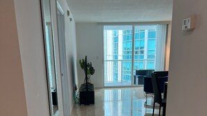 A spacious living area with a large window, a dining area with chairs, and a plant in the center. - *New* Elegant Apt Brickell 5 min. From Beach (Miami)