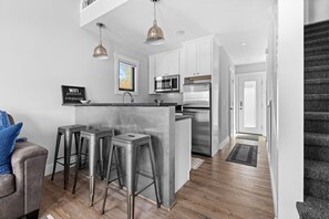 A modern kitchen with stainless steel appliances, a bar area with stools, and a grey and white color scheme.