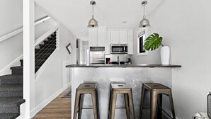 A modern kitchen with white cabinets, stainless steel appliances, and a central island with stools. - TC Loft Near Downtown w/ Open Layout (Traverse City)