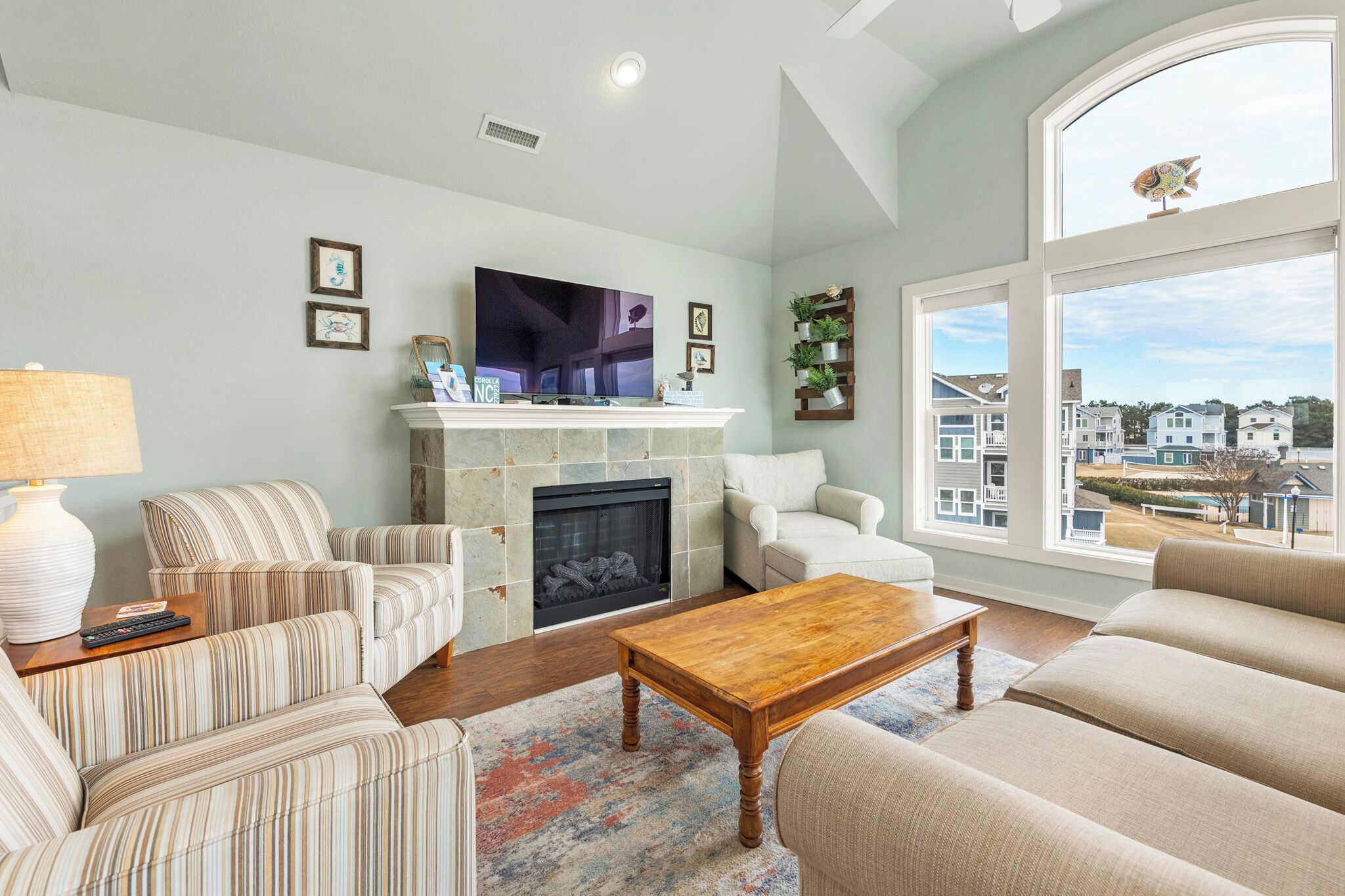 A living room with striped sofas, a fireplace, a TV, and a large window with a view of houses.