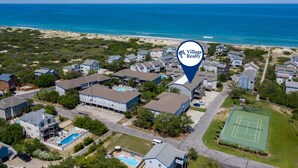 An aerial view of a residential area with houses, a tennis court, and a beach in the background. - Beach Place: Oceanside | Short Walk to the Beach (Corolla)