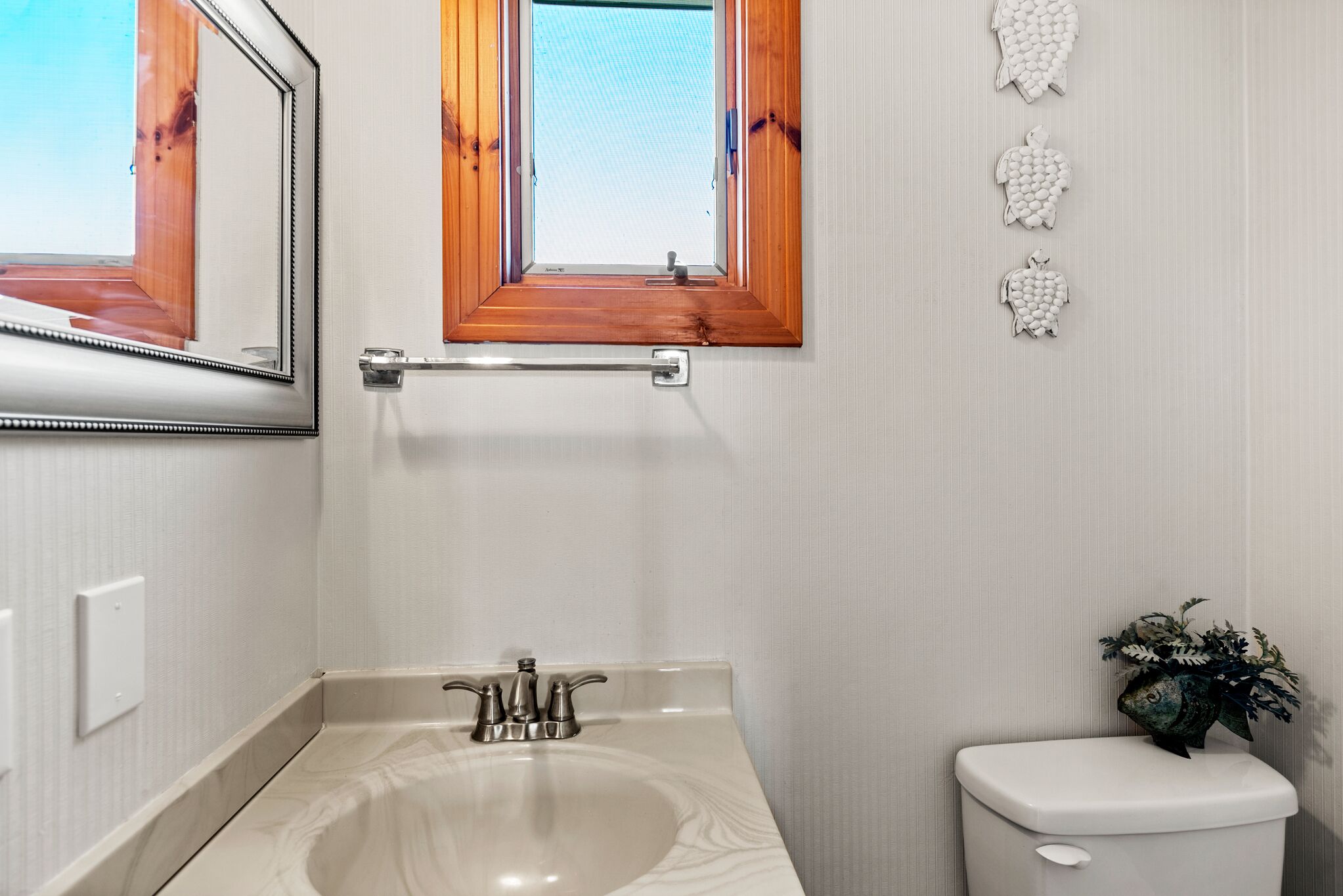Une salle de bain avec un lavabo blanc, des toilettes, une fenêtre avec des volets en bois et un miroir.