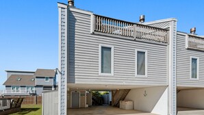 A two-story house with a covered garage, a fenced yard, and a staircase leading to the upper floor. - SeaFinn: Semi-Oceanfront | Pool Access | Dogs OK (Nags Head)