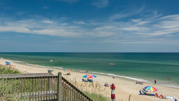 A beach with a wooden walkway, umbrellas, and people relaxing. - SeaFinn: Semi-Oceanfront | Pool Access | Dogs OK (Nags Head)