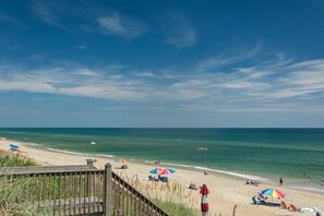 A beach with a wooden walkway, umbrellas, and people relaxing.