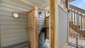 A wooden outdoor shower enclosure with a hose and a faucet. - SeaFinn: Semi-Oceanfront | Pool Access | Dogs OK (Nags Head)