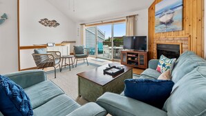 A spacious living room with a large TV, a fireplace, and a view of the outdoors. - SeaFinn: Semi-Oceanfront | Pool Access | Dogs OK (Nags Head)