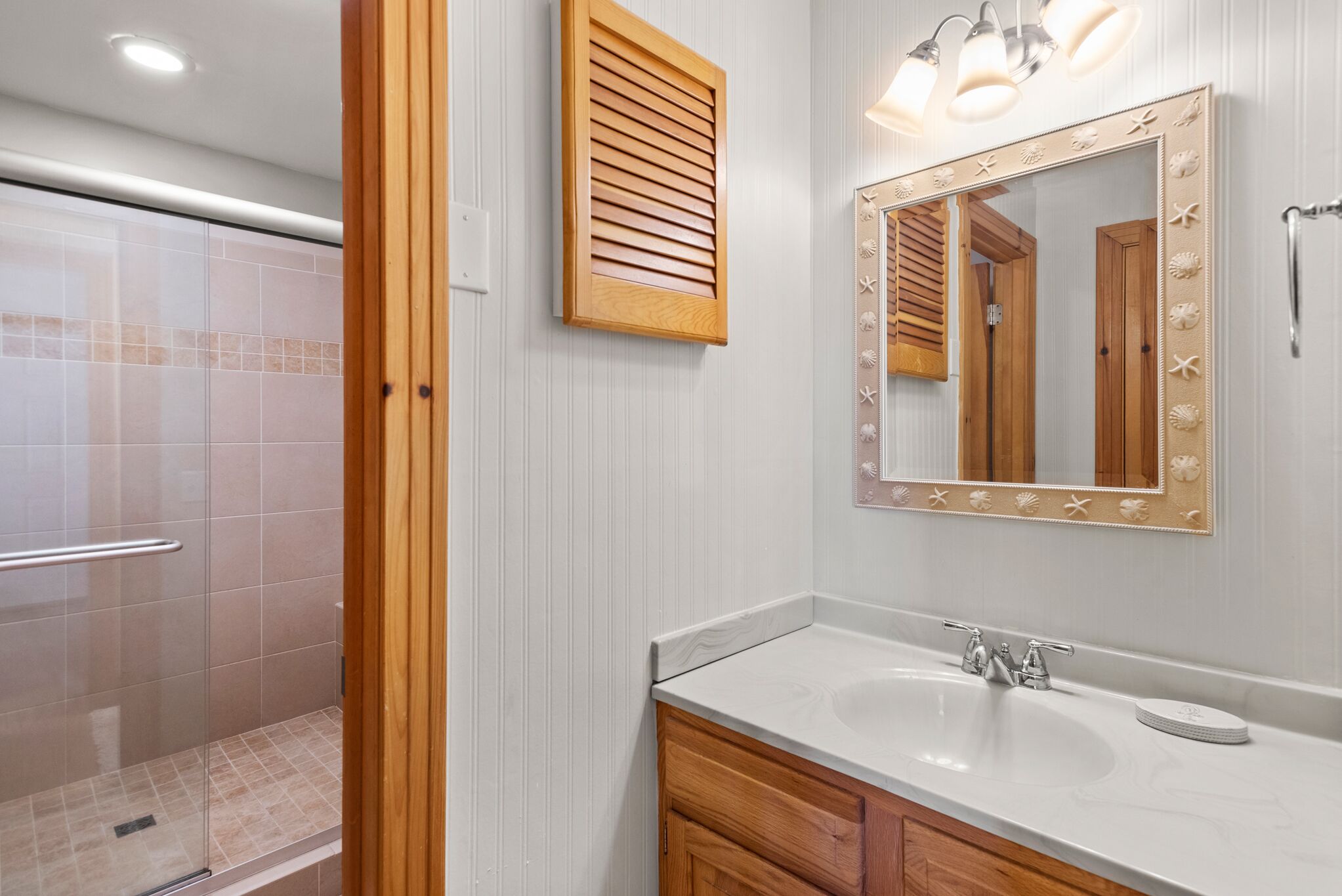 Un baño con ducha, un lavabo con tocador y un espejo con detalles decorativos.