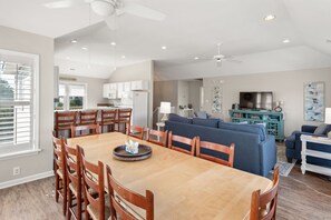 Uma sala de estar espaçosa com uma mesa de jantar, cadeiras, um sofá e uma televisão.