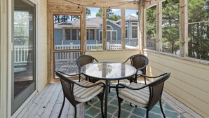 A covered patio with a round table and four chairs, overlooking a residential area with a wooden deck and a house. - Plum Paws: Pool | Hot Tub | Sound Views | Dogs OK (Corolla)