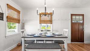Un comedor con una mesa blanca dispuesta para cuatro personas, una araña y una puerta de madera.