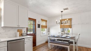 Una cocina con armarios blancos, encimera de madera y un comedor con mesa y sillas.