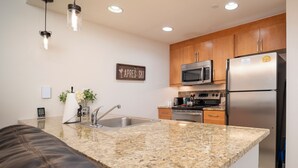 A modern kitchen with granite countertops, stainless steel appliances, wooden cabinets, and pendant lighting. - Fraser Crossing 3509 1 Bedroom modern and comfortable (Winter Park)
