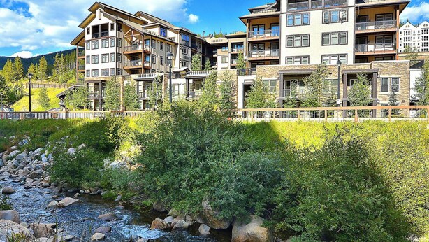 A multi-story hotel with balconies, a river in front, and a mountainous backdrop. - Fraser Crossing 3509 1 Bedroom modern and comfortable (Winter Park)