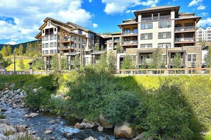 A multi-story hotel with balconies, a river in front, and a mountainous backdrop. - Fraser Crossing 1 Bedroom modern and comfortable (Winter Park)