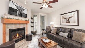 A living room with a fireplace, a leather sofa, a coffee table, a television, and a ceiling fan. - Fraser Crossing 3509 1 Bedroom modern and comfortable (Winter Park)