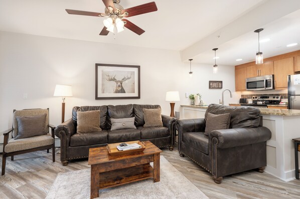 A living room with a brown leather sofa, a wooden coffee table, and a ceiling fan. - Fraser Crossing 1 Bedroom modern and comfortable (Winter Park)