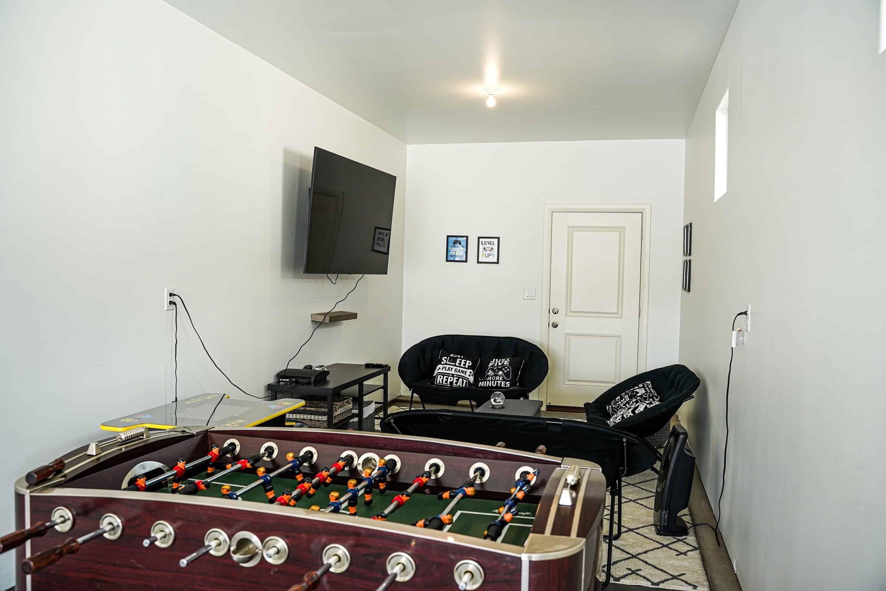 Une pièce avec une table de baby-foot, un téléviseur fixé au mur, une porte et une chaise avec un coussin.