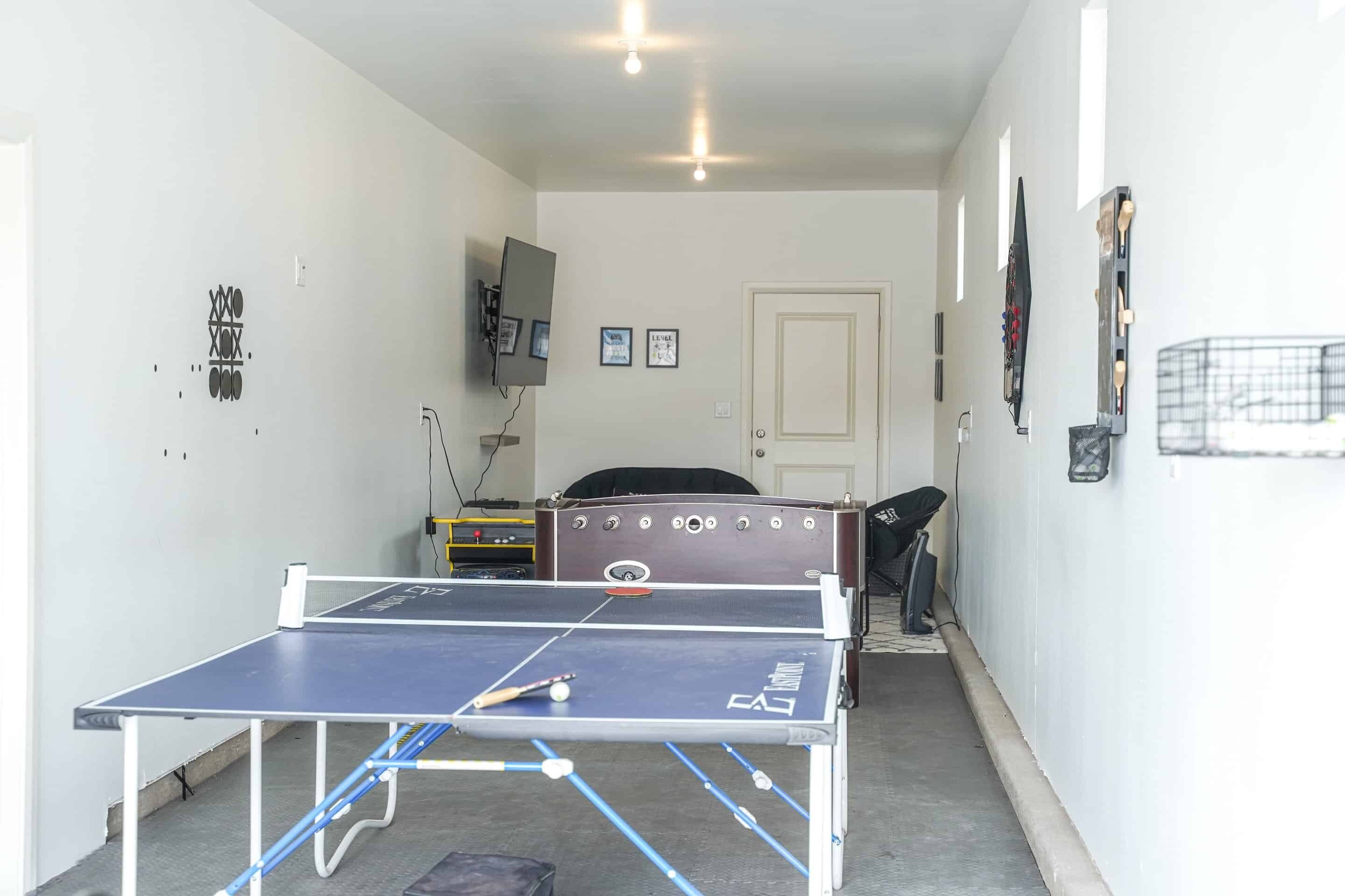 Een tafeltennistafel in een kamer met witte muren, een deur en een aan de muur bevestigde televisie.