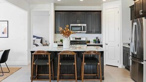 A modern kitchen with dark cabinets, stainless steel appliances, and a central island with bar stools. - Paseos to Redrocks, HUGE REC ROOM! PICKLEBALL! (Washington)