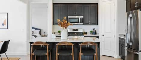 A modern kitchen with dark cabinets, stainless steel appliances, and a central island with bar stools.