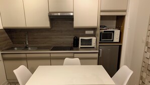 Een moderne keuken met een witte tafel en vier stoelen, een ingebouwde magnetron en een roestvrijstalen koelkast.