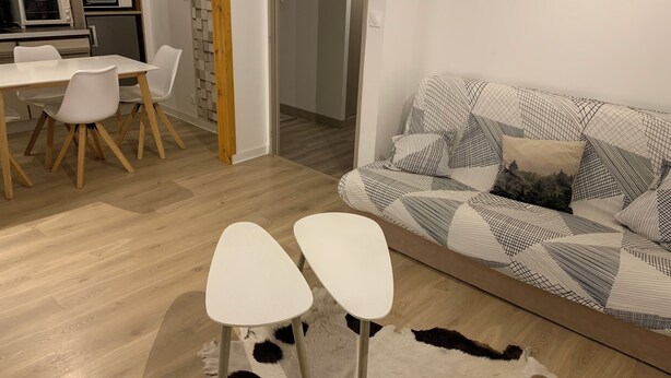 Een moderne woonkamer met een bank, twee witte stoelen, een eettafel en een keuken op de achtergrond.