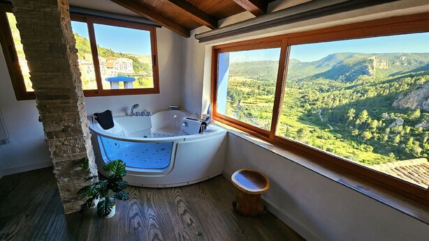 Une salle de bain dotée d’une grande baignoire, d’un banc en bois et offrant une vue sur un paysage montagneux.