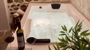 Une salle de bain avec un mur en pierre, une baignoire remplie d’eau, deux verres à vin et une bouteille de vin.