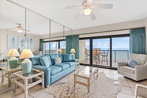A spacious living area with a blue sofa, glass coffee table, and a view of the ocean through large sliding doors. - The Palms 613 by Liquid Life (Orange Beach)