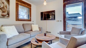 Un salon moderne avec un canapé gris, une table basse ronde et un téléviseur fixé au mur.
