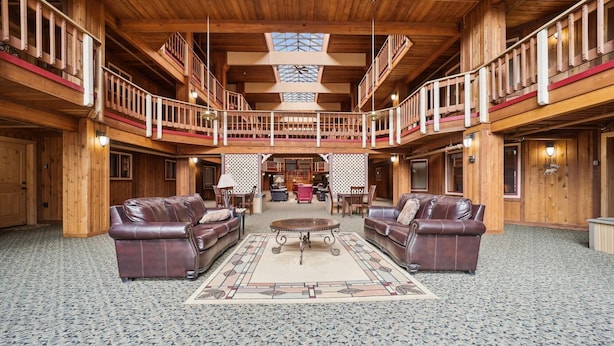 A spacious lobby with a high ceiling, wooden railings, and a central seating area with leather sofas and a patterned rug.