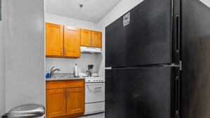 A compact kitchen with wooden cabinets, a black refrigerator, a stainless steel trash can, and a white stove.