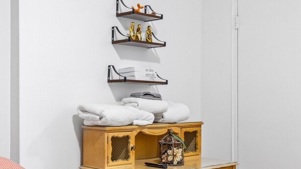 A bedroom with a wooden nightstand, a white bed, and a white wall.