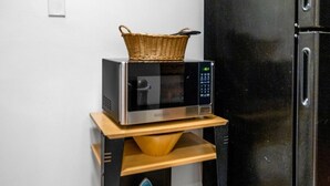A kitchen with a microwave on a wooden shelf, a basket on top, and an iron on the lower shelf.